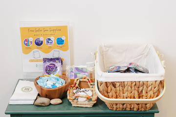 Display of free safer-sex supplies, including condoms, oral dams, lubricant packets, and informational materials arranged in baskets on a green table at the Center for Wellness and Health Promotion.