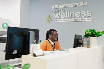 Reception area with a smiling staff member behind a white desk beneath a “David S. Rosenthal M.D. Center for Wellness” sign.